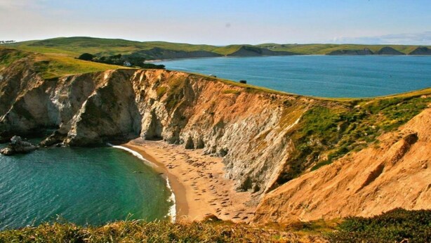 A coastal landscape with cliffs, a beach, and a body of water.
