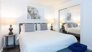 A neatly arranged bedroom with a large bed, two bedside tables with lamps, patterned pillows, a mirror, and a framed picture on the wall.