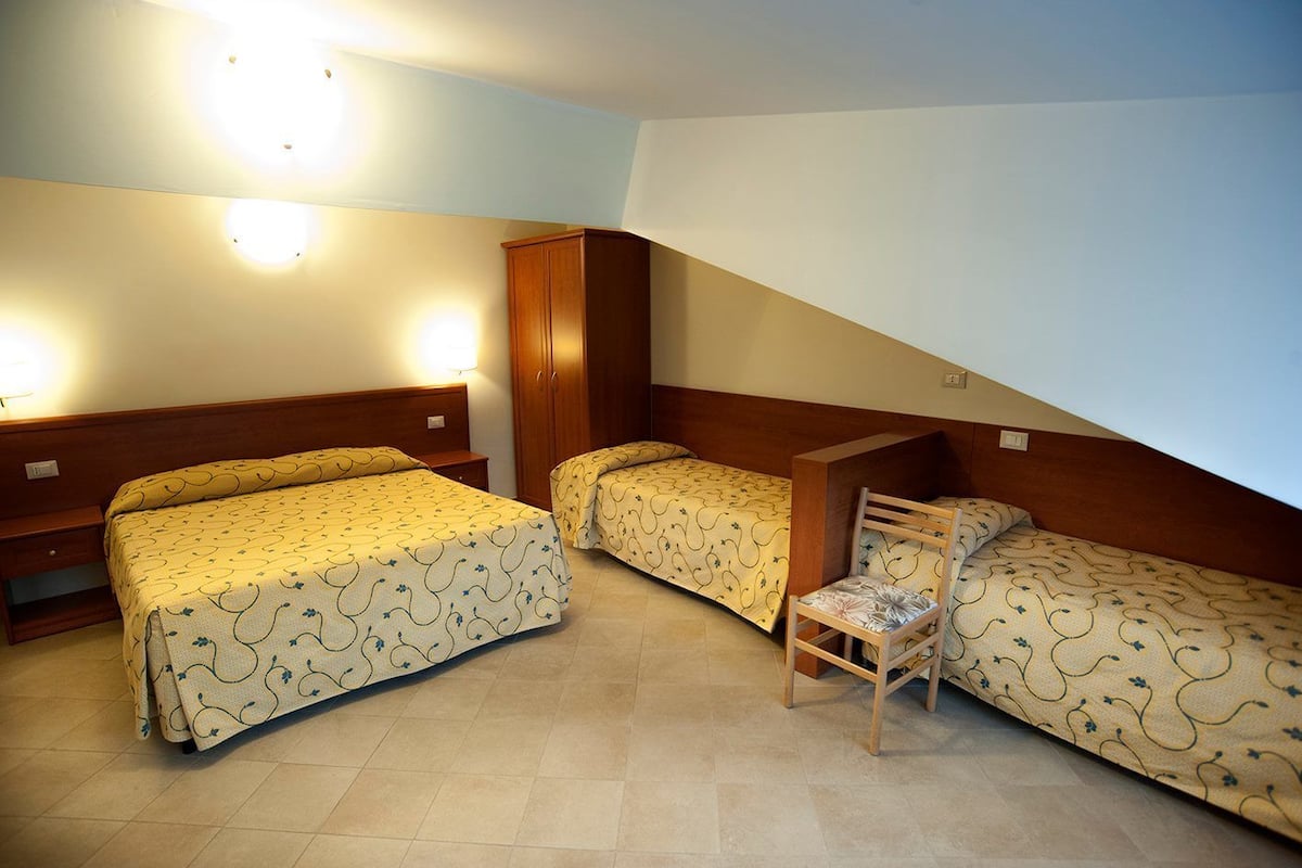 Una habitación con tres camas, un armario de madera y una silla.
