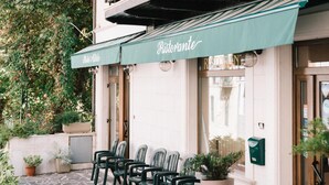 Un restaurante con terraza al aire libre, toldo verde y patio empedrado de piedra.