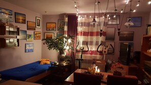 A cozy room with a bed, a desk, and a dining area. There are multiple framed pictures on the walls, a plant, and a curtain with a striped pattern. - Lakeside Smoker Apartment FDH (Friedrichshafen)