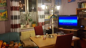 A living room with a sofa, a table with a lamp, a TV, and various decorations including plants and framed pictures. - Lakeside Smoker Apartment FDH (Friedrichshafen)