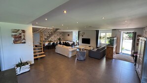 A spacious living area with a staircase, a dining area, a seating area with sofas, a television, and a kitchen area. - La Maison de Benjamin (La Chapelle-Saint-Aubert)