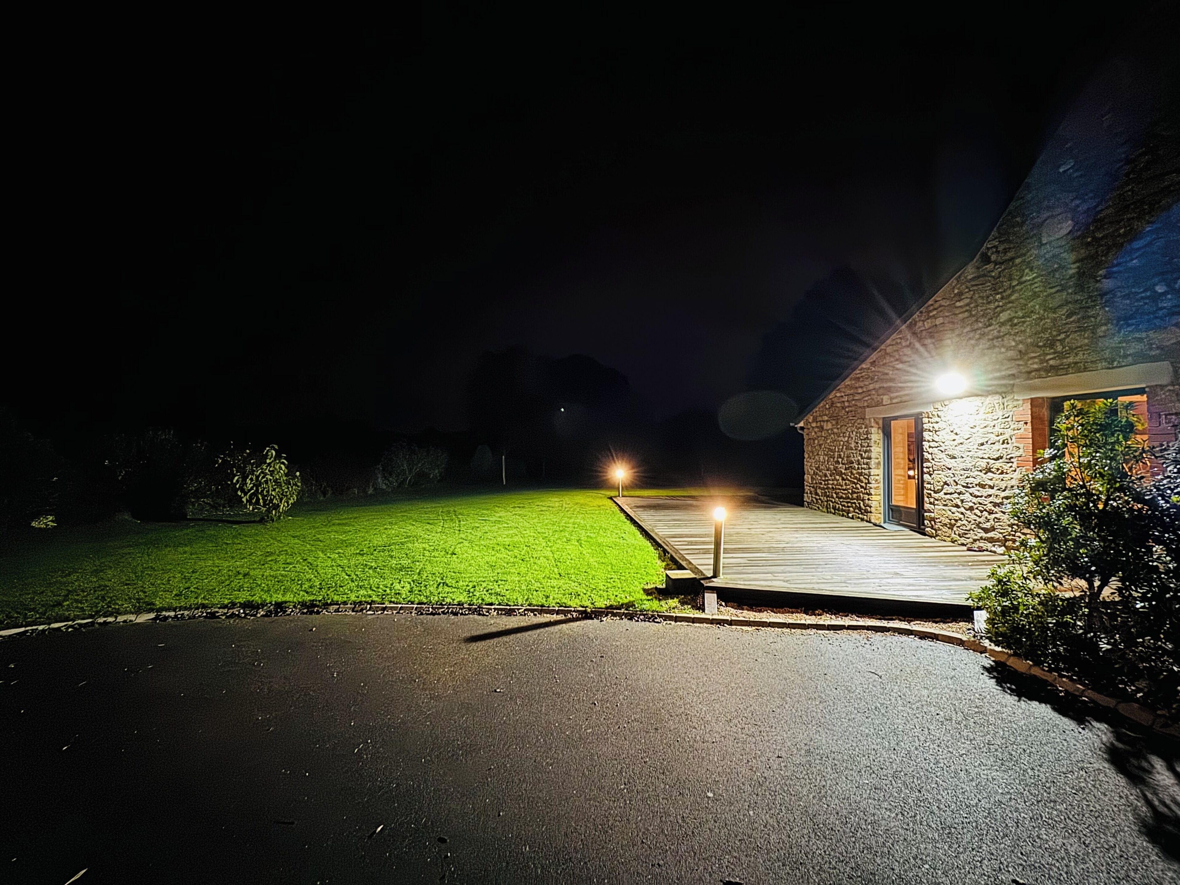 Vista nocturna de un edificio de piedra con una terraza de madera y un camino de entrada pavimentado.