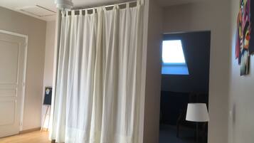 A bedroom with a bed, a white curtain, a ceiling fan, a window, and a painting on the wall.