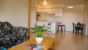 A living room with a sofa, a coffee table with books and a plant, a kitchen with cabinets and appliances, and a dining area with chairs.