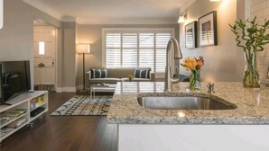 Una cocina moderna con encimera de granito, pileta de acero inoxidable y un comedor con sofá y mesa de centro.