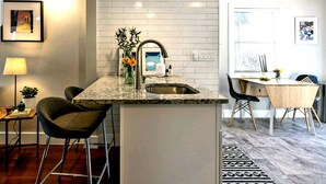 Una cocina moderna con encimera de granito, pileta de acero inoxidable y taburetes de bar.