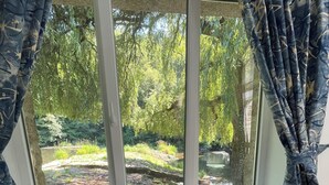 A wooden dining table with chairs, a vase with flowers, and a window with curtains. - Le Gite D'Ile (1 Bedroom, Sleeps 2) (Souleuvre En Bocage)
