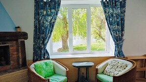 A room with a large window, two wicker chairs with green cushions, a small table, and a checkered floor. - Le Gite D'Ile (1 Bedroom, Sleeps 2) (Souleuvre En Bocage)