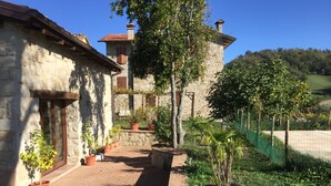 A stone building with a tiled roof, surrounded by potted plants and a grassy area. - Olimpia - Spacious stone villa with private terrace overlooking the pool (Bologna)