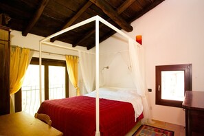 Een kamer met een hemelbed, een houten tafel en een raam met gordijnen.