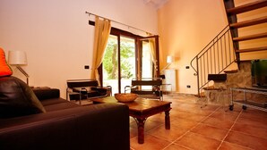 A spacious living room with a sofa, a wooden coffee table, and a dining table. A staircase with a wooden railing leads to an upper level. - Olimpia - Spacious stone villa with private terrace overlooking the pool (Bologna)
