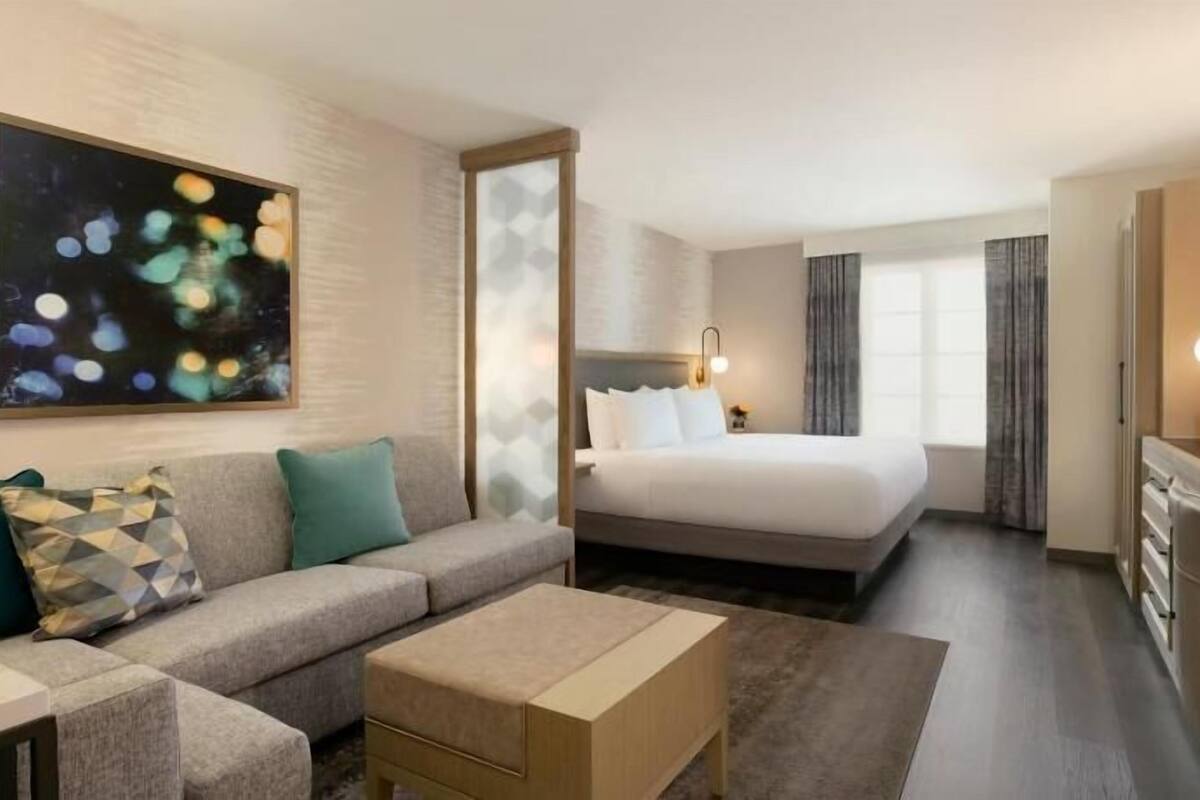 Quarto de hotel com cama, sofá, televisão e um quadro na parede.