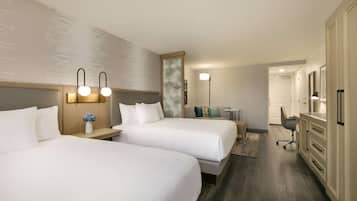 A hotel room with two beds, a desk, a chair, a dresser, and a lamp.