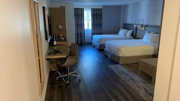 Habitación de hotel con dos camas, un escritorio con silla, televisor y ventana con cortinas.