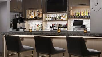 Un espace bar comprenant trois tabourets, un comptoir avec diverses bouteilles et verres, un téléviseur placé au-dessus du bar et un appareil à café.