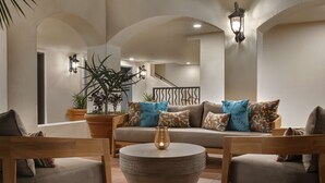 Uma sala de estar acolhedora com uma mesa de centro redonda, cadeiras de madeira, um sofá com almofadas estampadas e plantas em vasos.