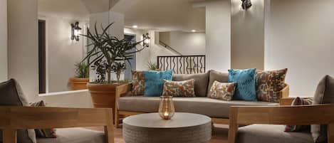 Una sala acogedora con una mesita redonda, sillas de madera, un sofá con cojines estampados y plantas en macetas.