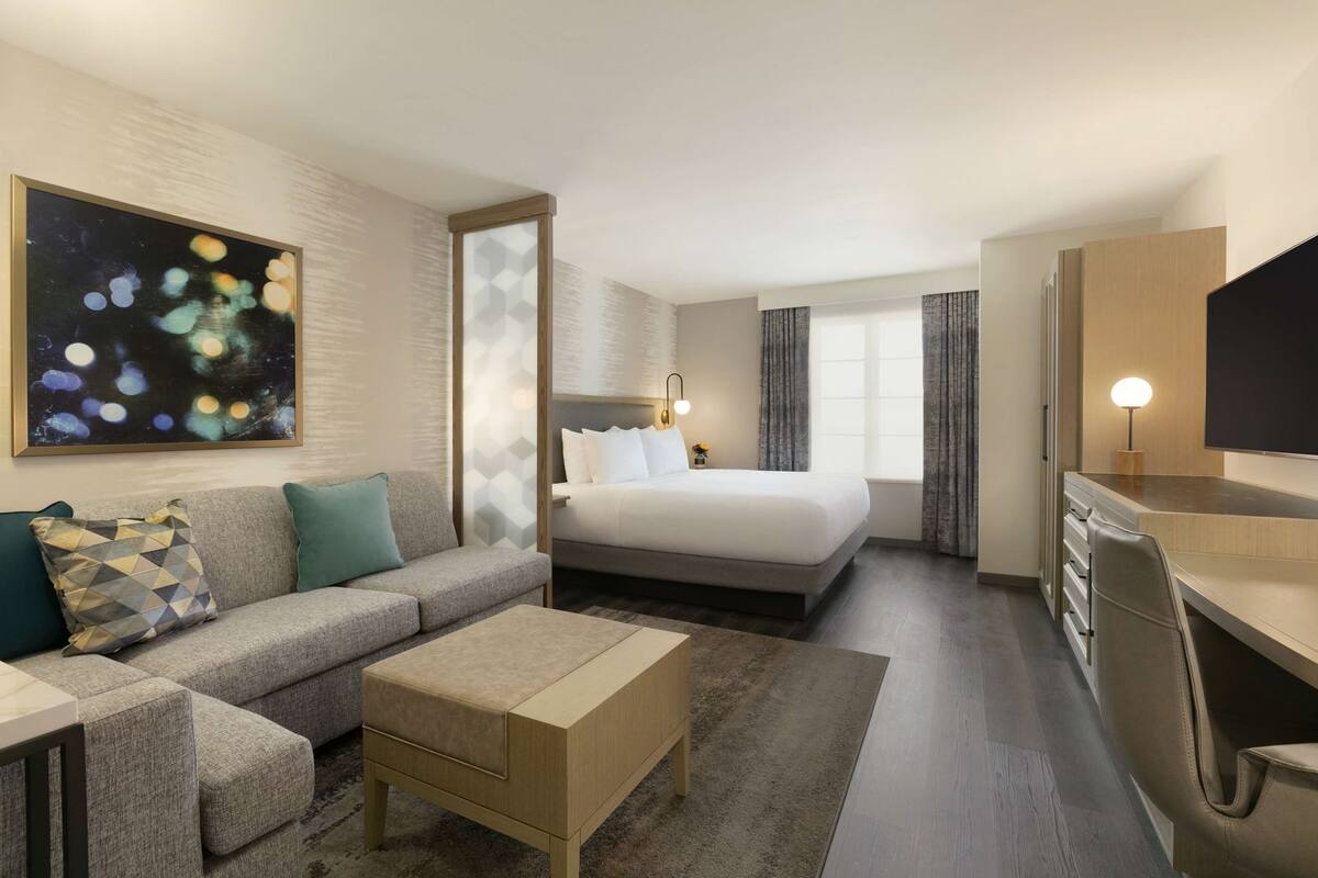 Quarto de hotel moderno com sofá, cama, escrivaninha e televisão.