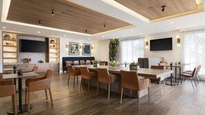 Uma sala de jantar moderna com uma mesa comprida, várias cadeiras, uma televisão e uma planta.