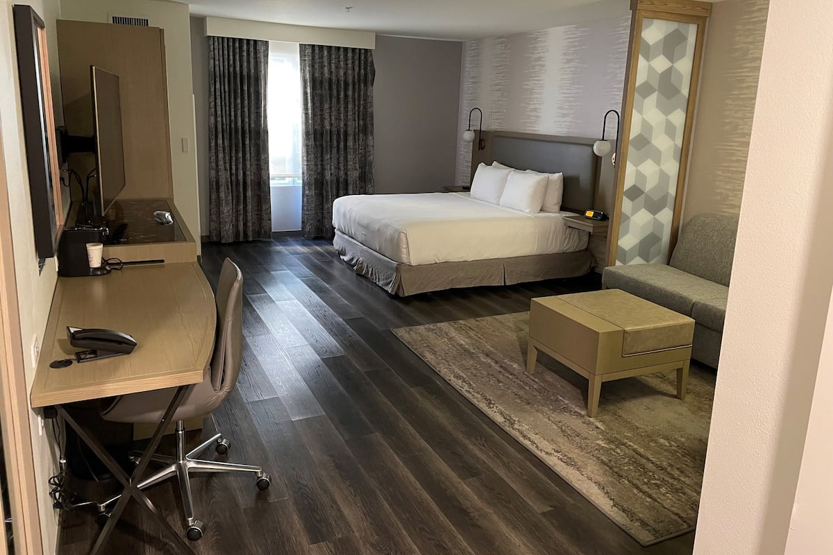 Quarto de hotel com cama, escrivaninha, cadeira e uma pequena mesa.