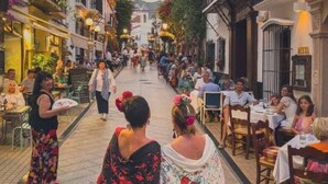 Una calle con terrazas de cafés, una acera y edificios con balcones.