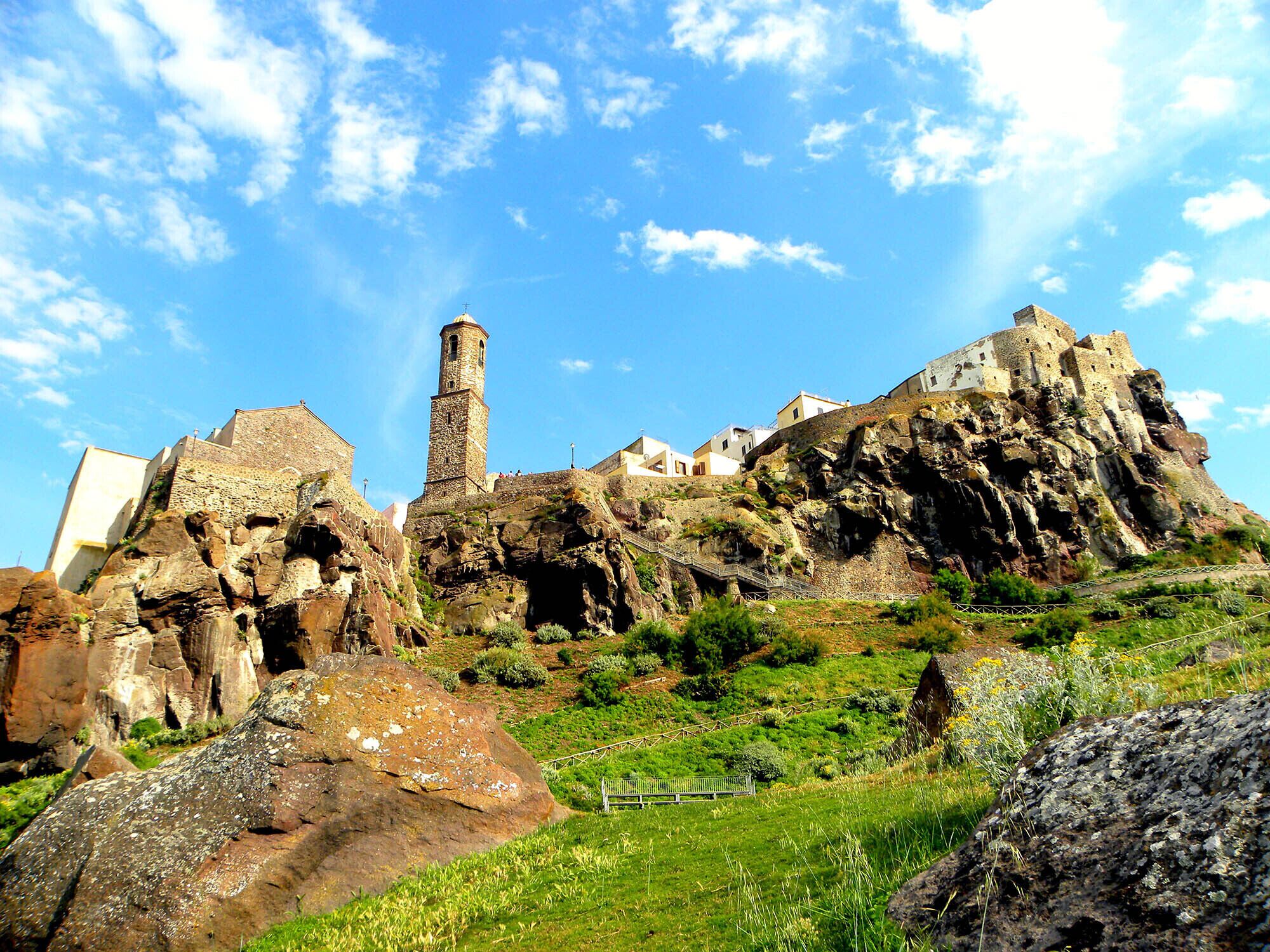 A historic stone building with a prominent tower, situated on a rocky hillside with a clear sky.