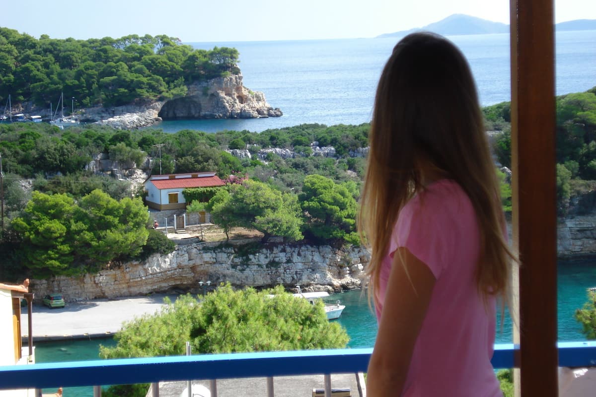 A balcony with a view of a coastal area, including a rocky outcrop and a small building with a red roof.