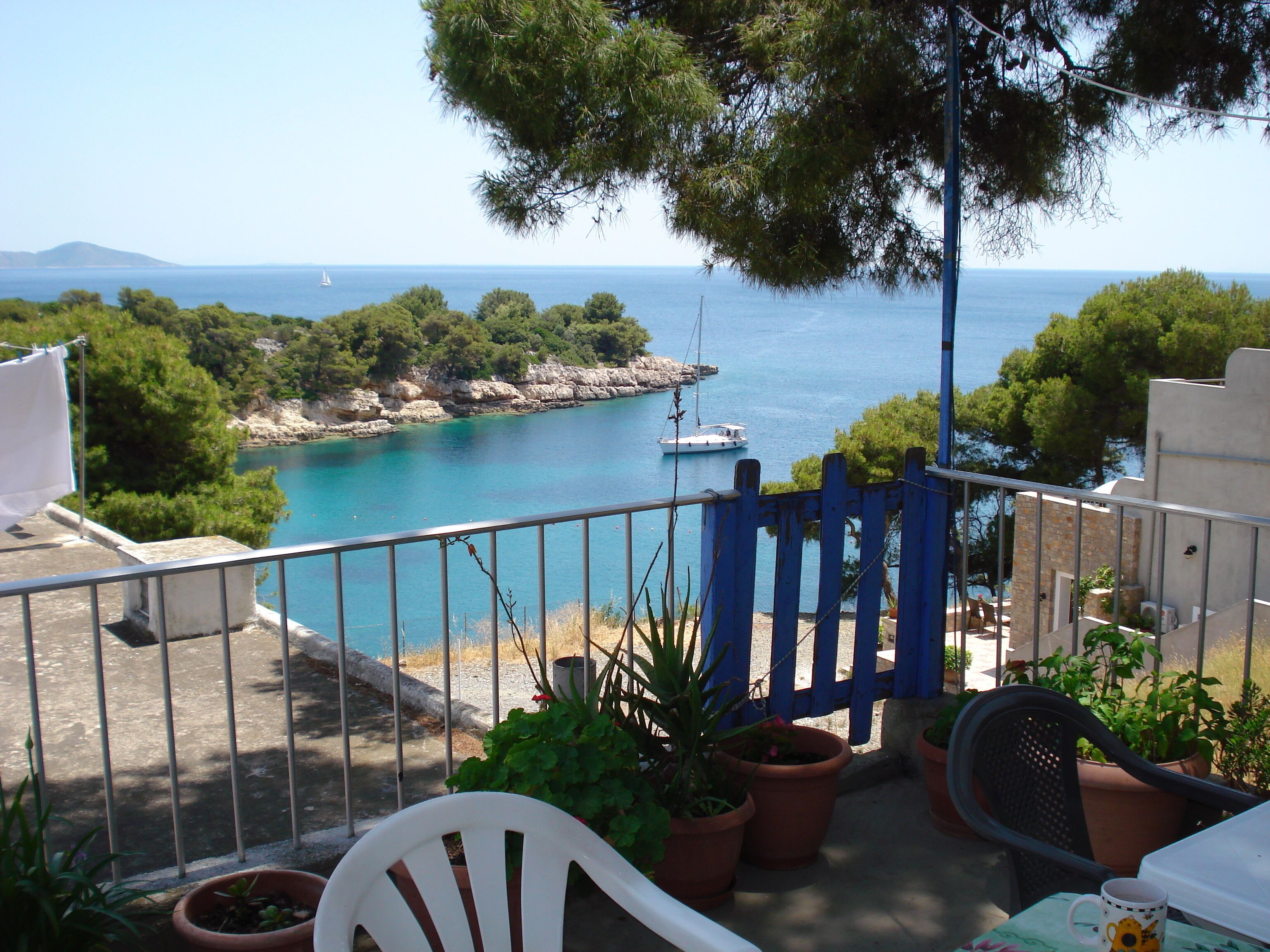 A balcony with a view of the sea, potted plants, and outdoor furniture.