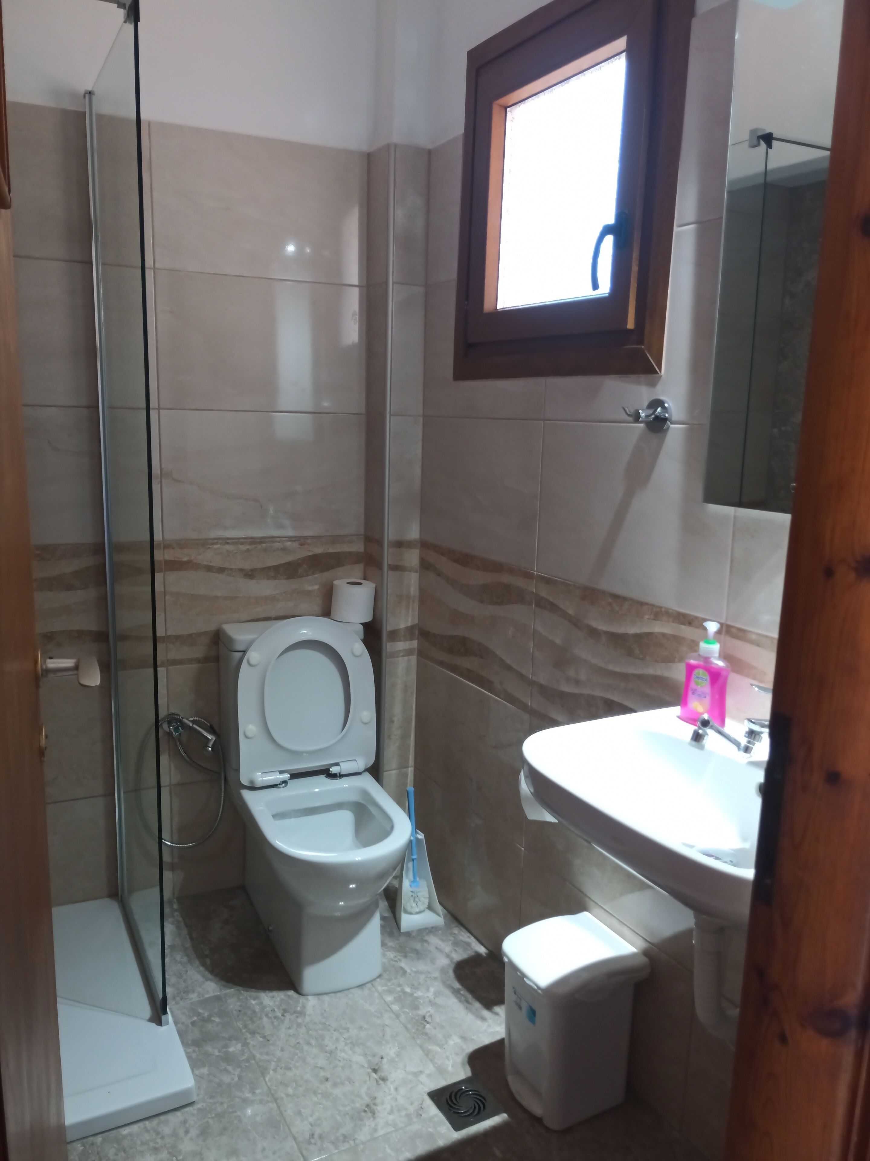 Ein Badezimmer mit Toilette, einer Duschkabine aus Glas, einem Waschbecken und einem kleinen Mülleimer.
