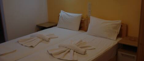 A neatly made bed with towels arranged in a bow shape, a bedside table, and a nightstand with a lamp.