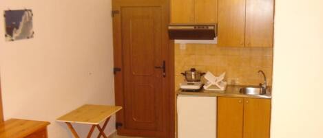 A compact kitchen with wooden cabinets, a sink, a stove, and a small table.