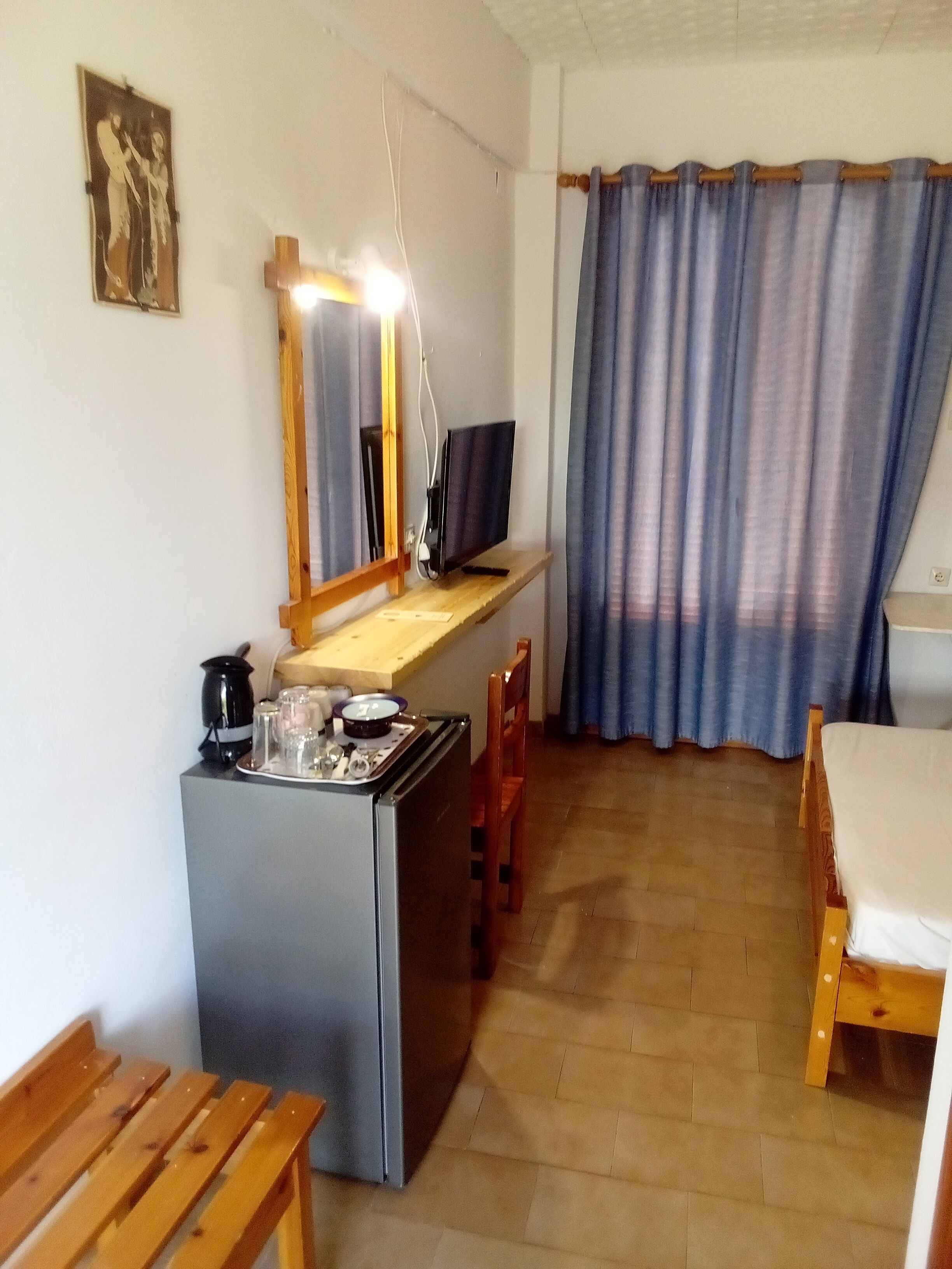 Quarto compacto com cozinha compacta, uma cama, um banco de madeira e uma janela grande com cortinas.