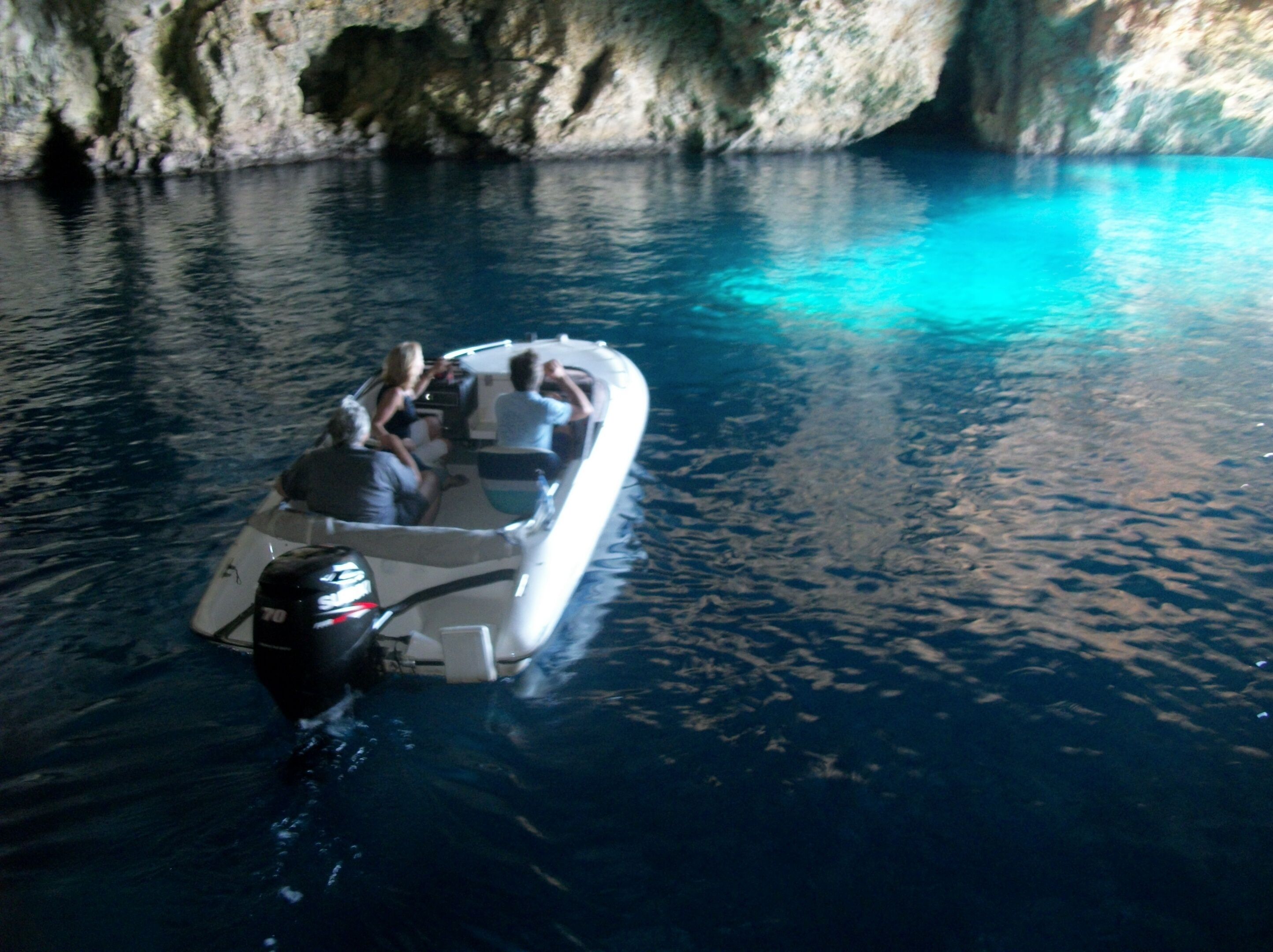 A boat with passengers on a calm body of water near a rocky cliff.