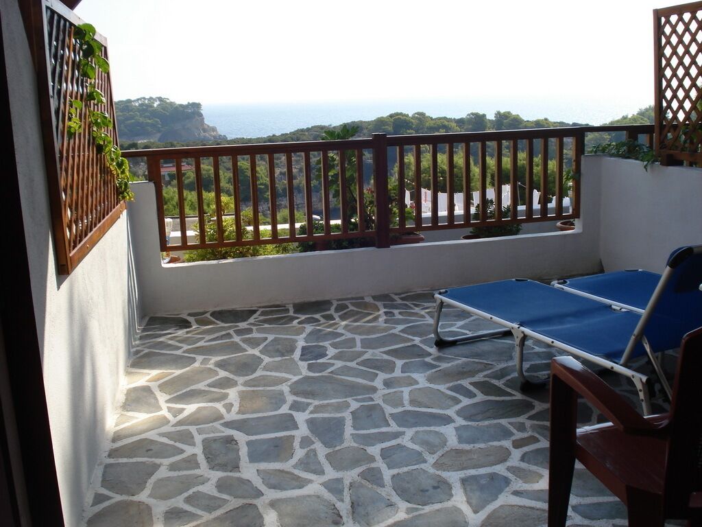 A stone-floored balcony with a view of the sea, a pool table, and a wooden chair.