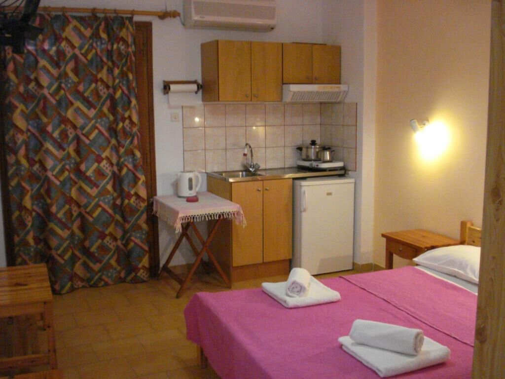 A small, cozy room with a bed, a table, a kitchenette, and a shower area.