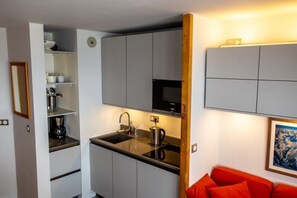 Une cuisine compacte avec un plan de travail noir, un évier et un four à micro-ondes. Un canapé rouge se trouve dans le salon attenant.