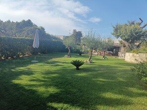 A well-maintained garden with a lawn, a few trees, and a patio area with outdoor furniture.