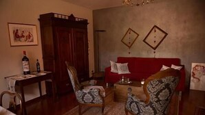 Una sala de estar con un sofá rojo, dos sillones estampados, un aparador de madera y una mesita con una botella.
