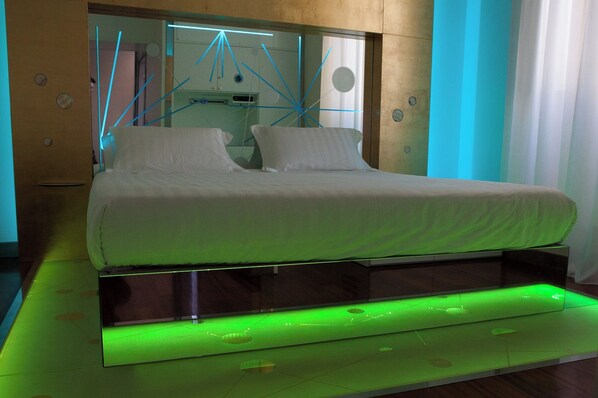 A modern bed with a metallic frame and green underbed lighting, a large mirror with geometric patterns, and a wall with circular cutouts. - Hotel Trecento (Rome)