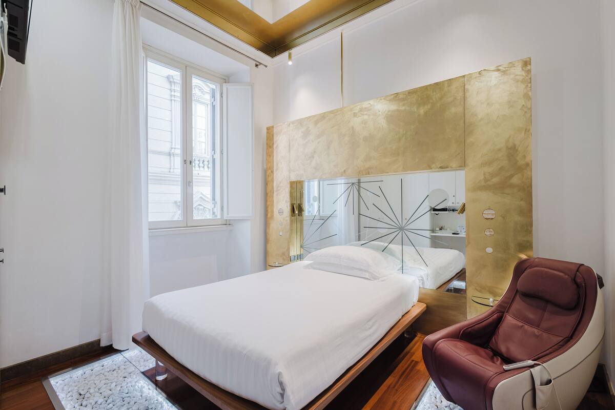 A modern bedroom with a bed, a massage chair, and a large mirror with a gold frame.