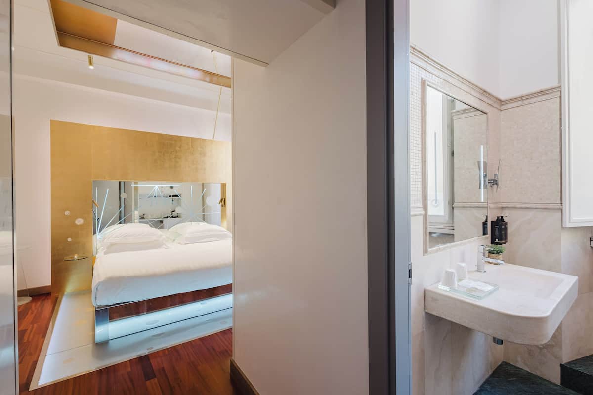 A modern hotel room with a bed, bedside table, and a bathroom with a sink and mirror.