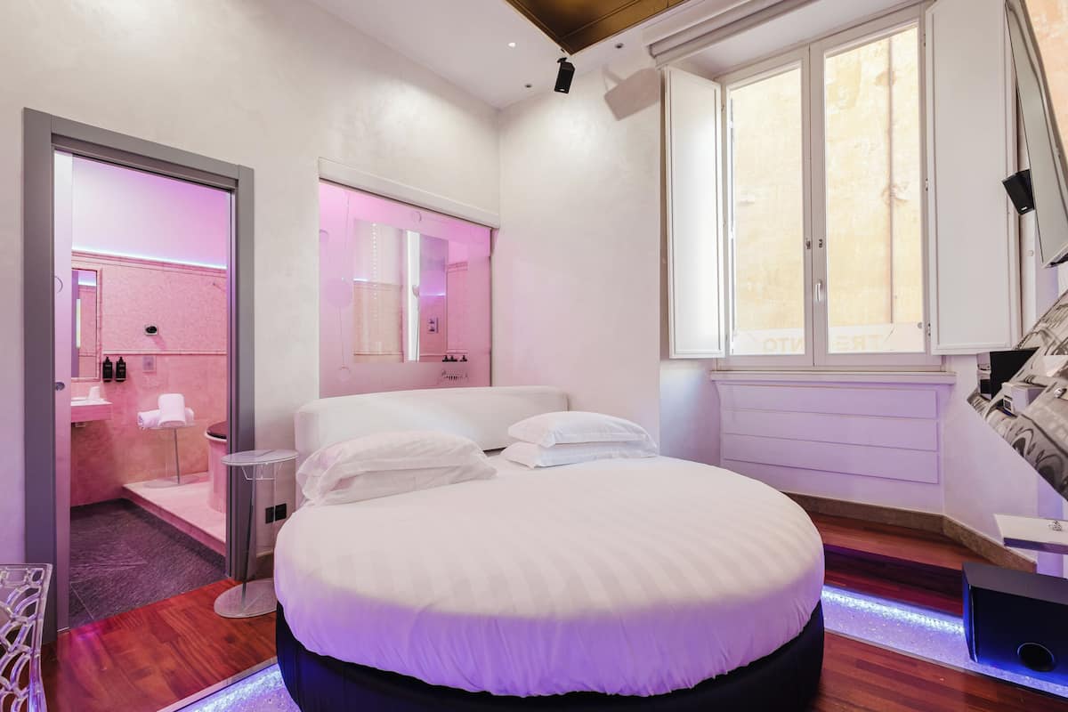 A modern bedroom with a large bed, a vanity with a mirror, and a window with blinds.