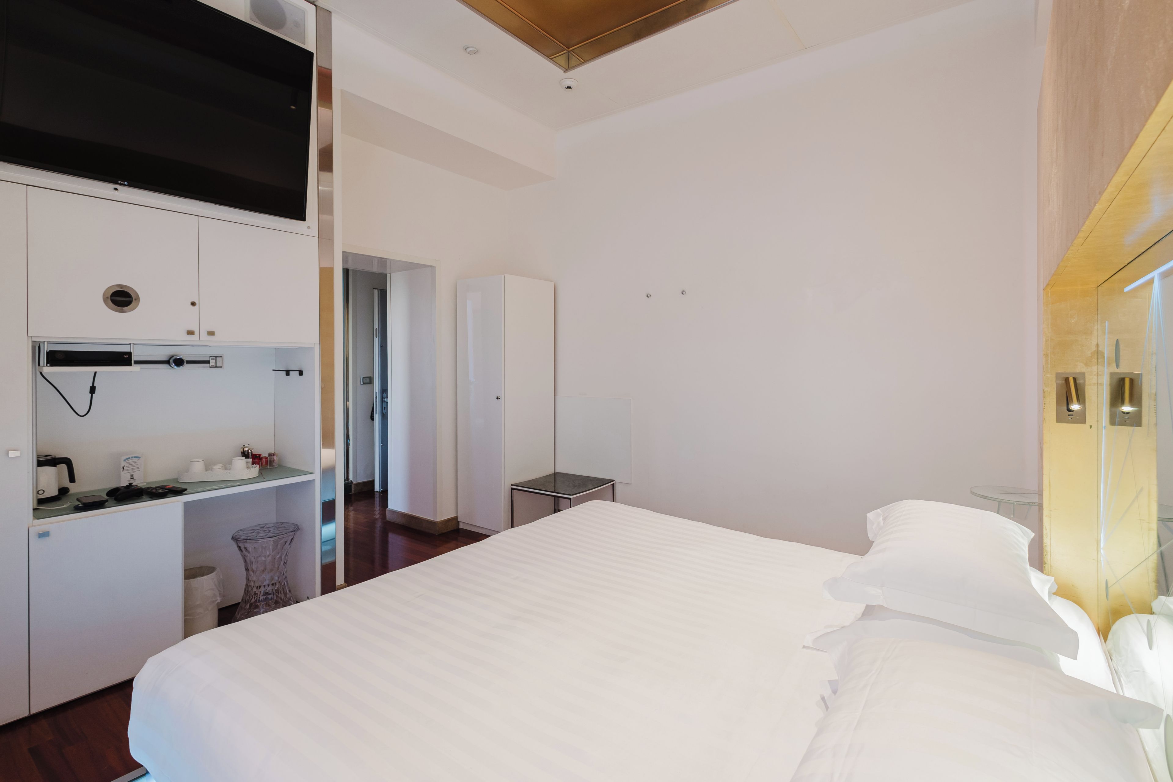 A modern hotel room with a large bed, a kitchenette, a small table, and a mirror.