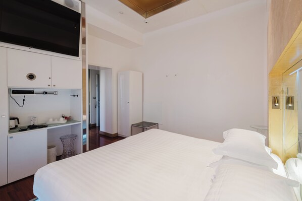 A modern hotel room with a large bed, a kitchenette, a small table, and a mirror.