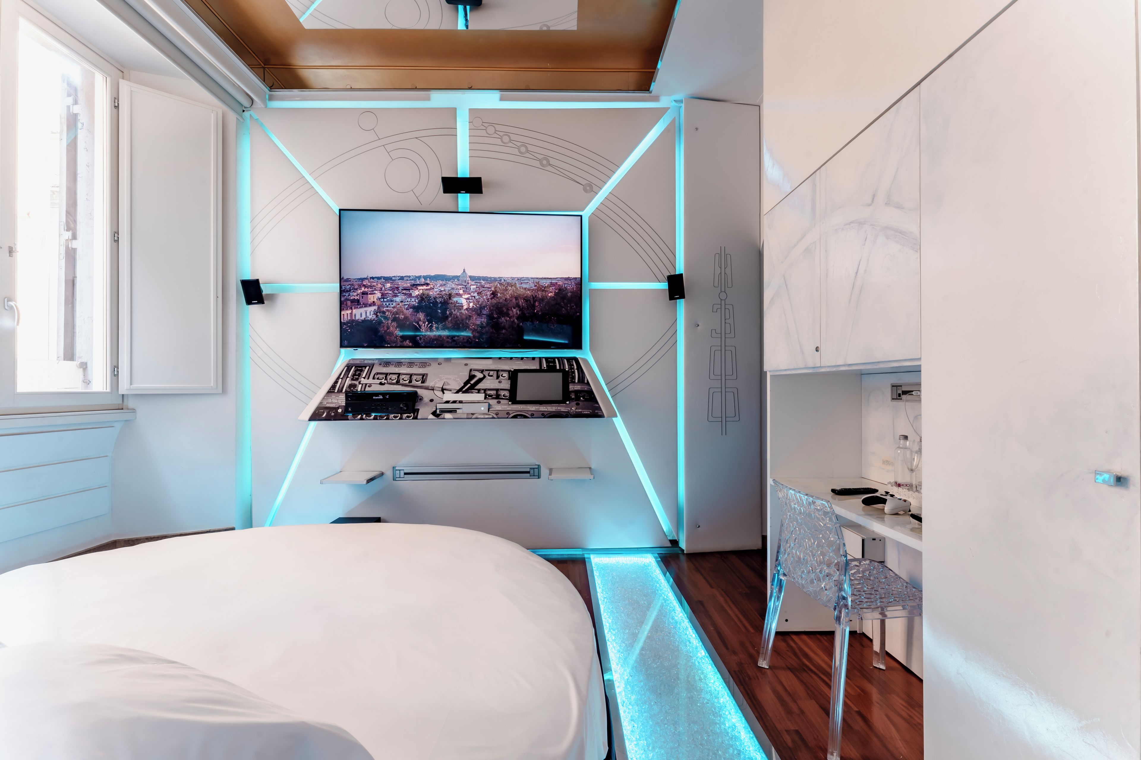 A modern bedroom with a large bed, a desk with a computer, and a TV mounted on the wall.