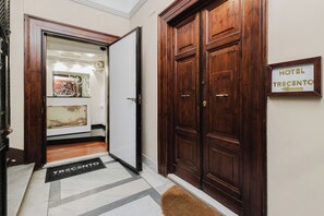 A hotel entrance with a wooden door, a sign indicating 'HOTEL TRECENTO', and a doormat with the hotel's name.