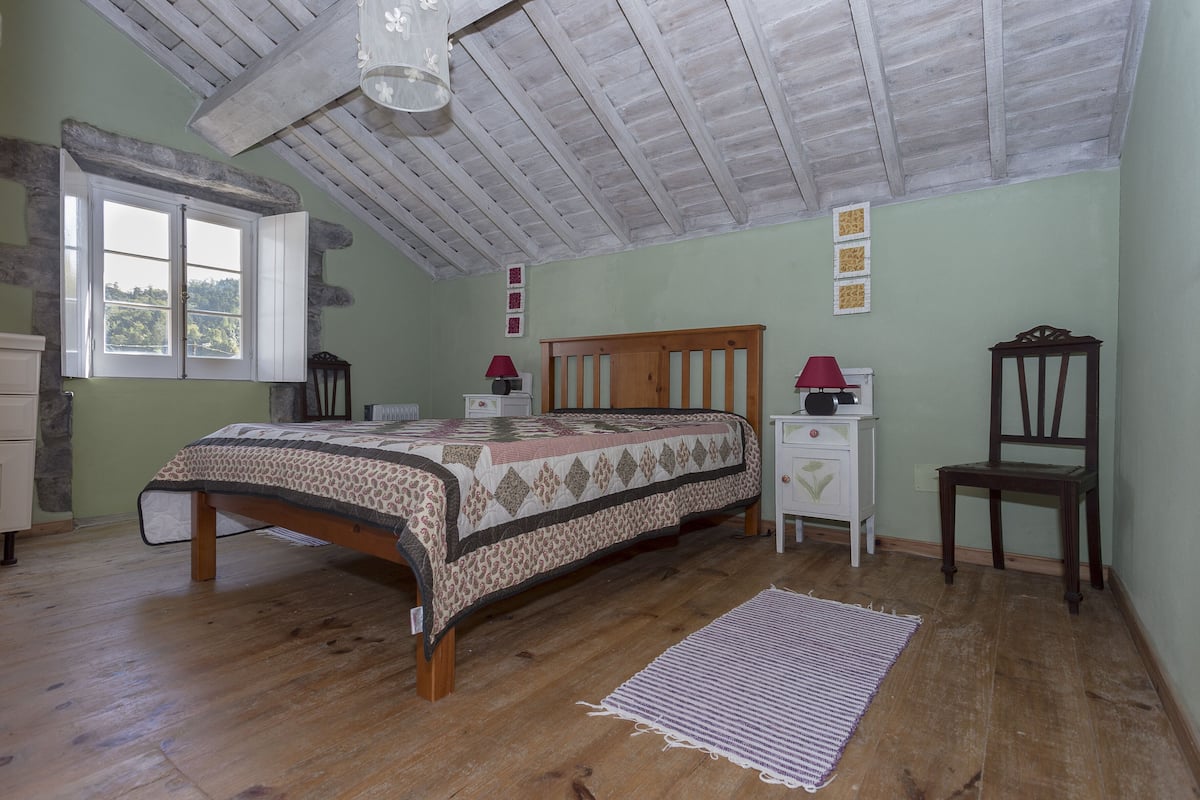 A bedroom with a wooden bed, a nightstand, a chair, a window with a view, and a ceiling fan.