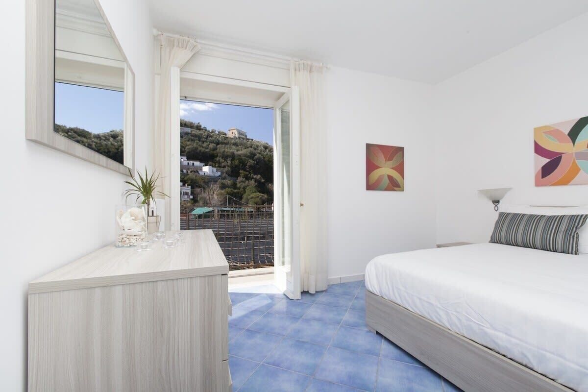 Une chambre à coucher avec un lit, une commode, une fenêtre avec des rideaux et un tableau accroché au mur.